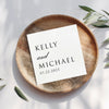 A white square card with black text is placed on a wooden plate, surrounded by leaves.
