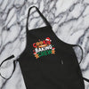A black apron with a festive design, featuring the text "COOKIE BAKING CREW" and images of cookies and gingerbread men.