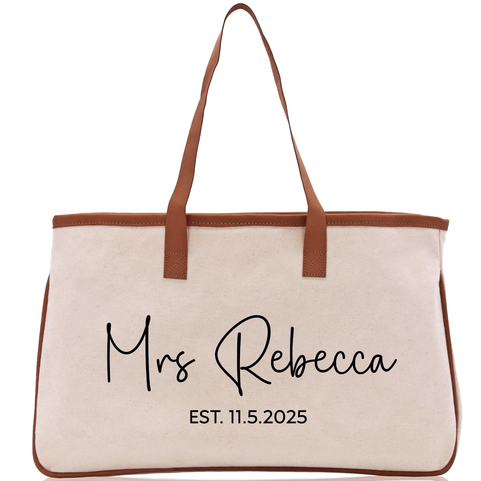 A beige canvas tote bag with brown straps and the text &quot;Mrs Rebecca EST. 11.5.2025&quot; printed on it.