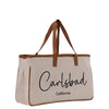 A beige canvas tote bag with brown straps and the text "Carlsbad, California" printed on it.