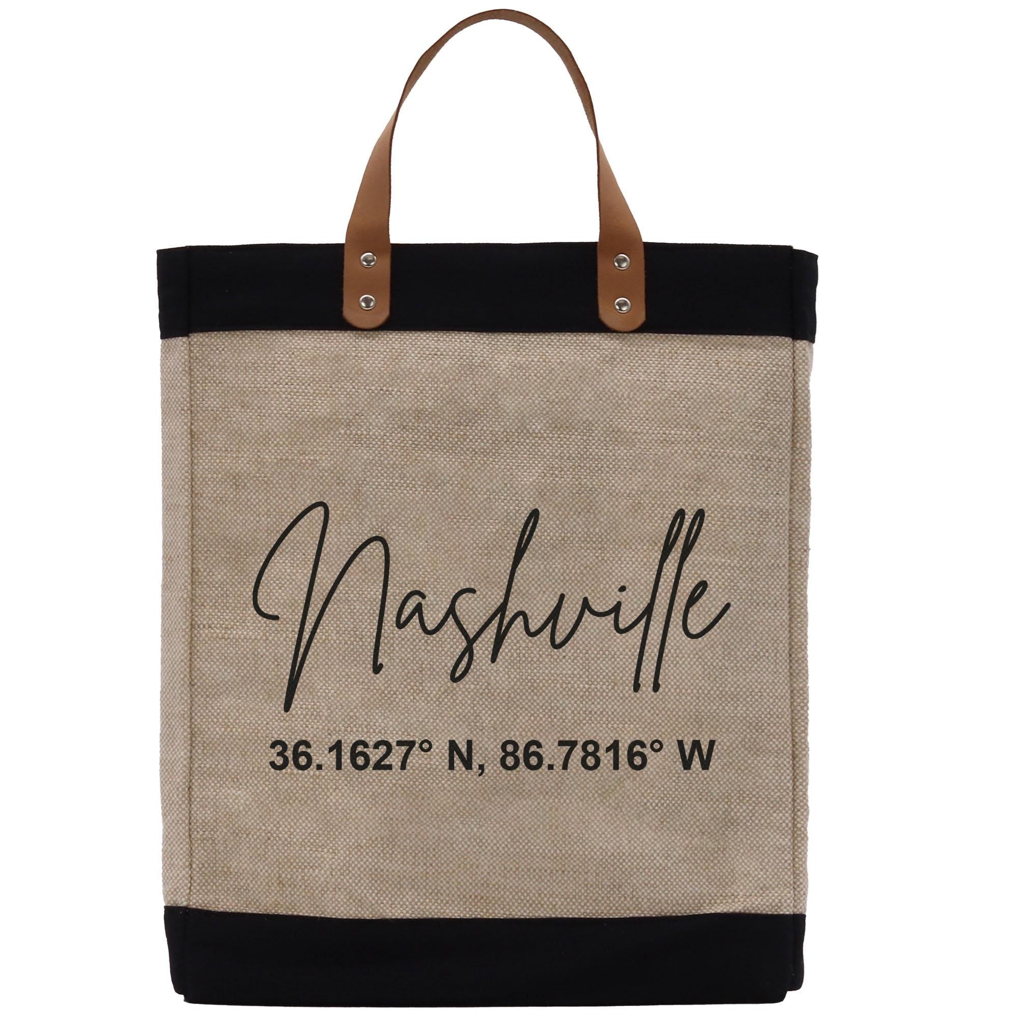 A beige tote bag with black trim and leather handles, featuring the text &quot;Nashville&quot; and a coordinate pair &quot;36.1627 N, 86.7816 W&quot; printed on it.