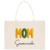 A white tote bag with the word "MOM" printed in large yellow letters and the name "Savannah" written below in smaller black letters.