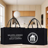 Two black tote bags with text and logos printed on them, placed on a wooden surface in a room with a kitchen visible in the background.