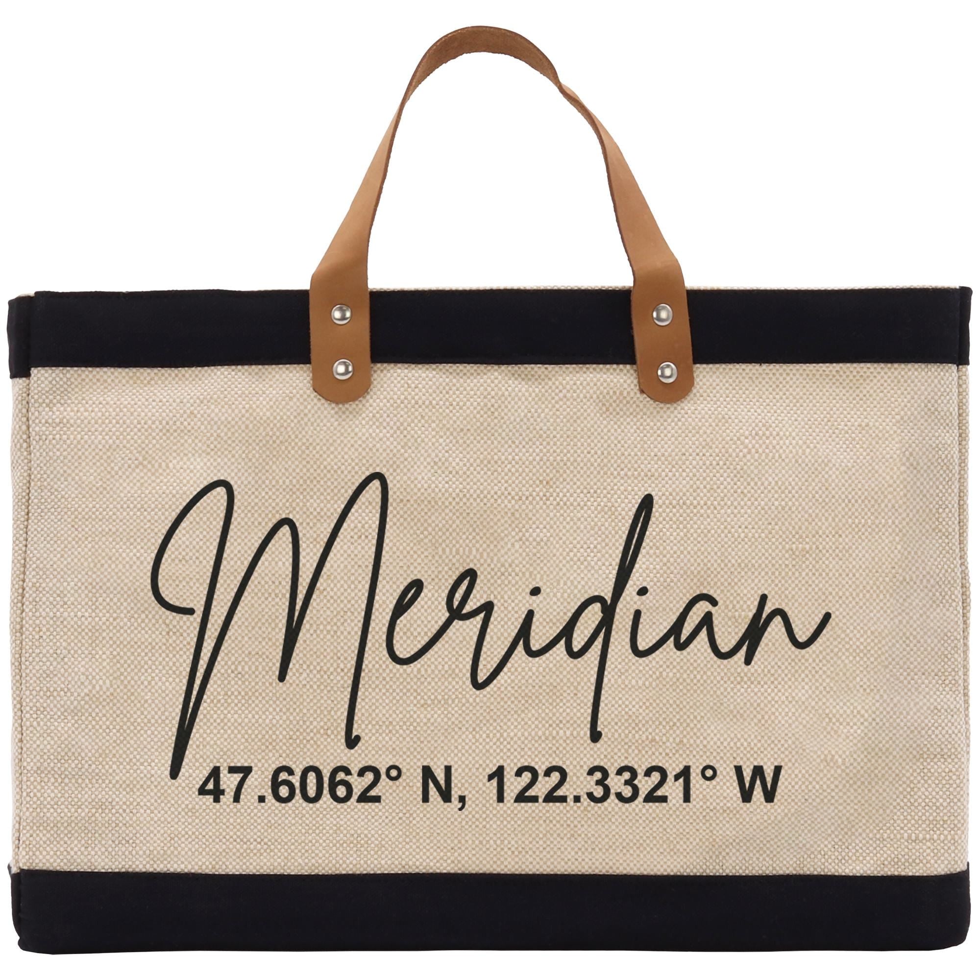 A beige tote bag with black trim and leather handles, featuring a personalized name and location printed on it.