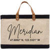 A beige tote bag with black trim and leather handles, featuring a personalized name and location printed on it.