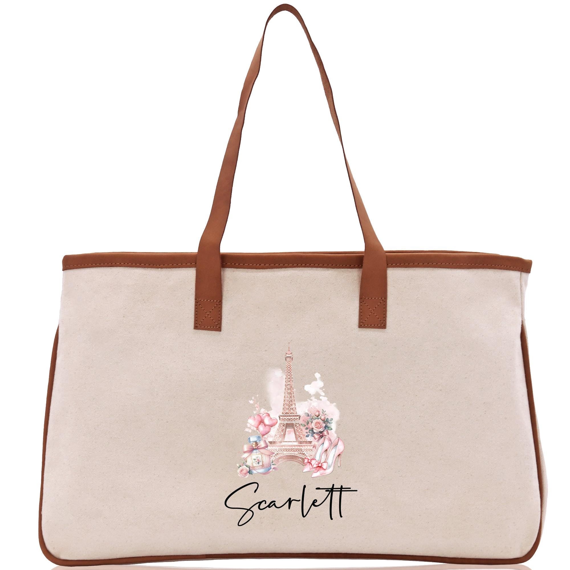 A beige canvas tote bag with a brown leather strap and a printed image of the Eiffel Tower on it.