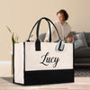 A large white tote bag with the name "Lucy" printed on it, placed on a wooden floor in a room with a woman sitting on a couch in the background.