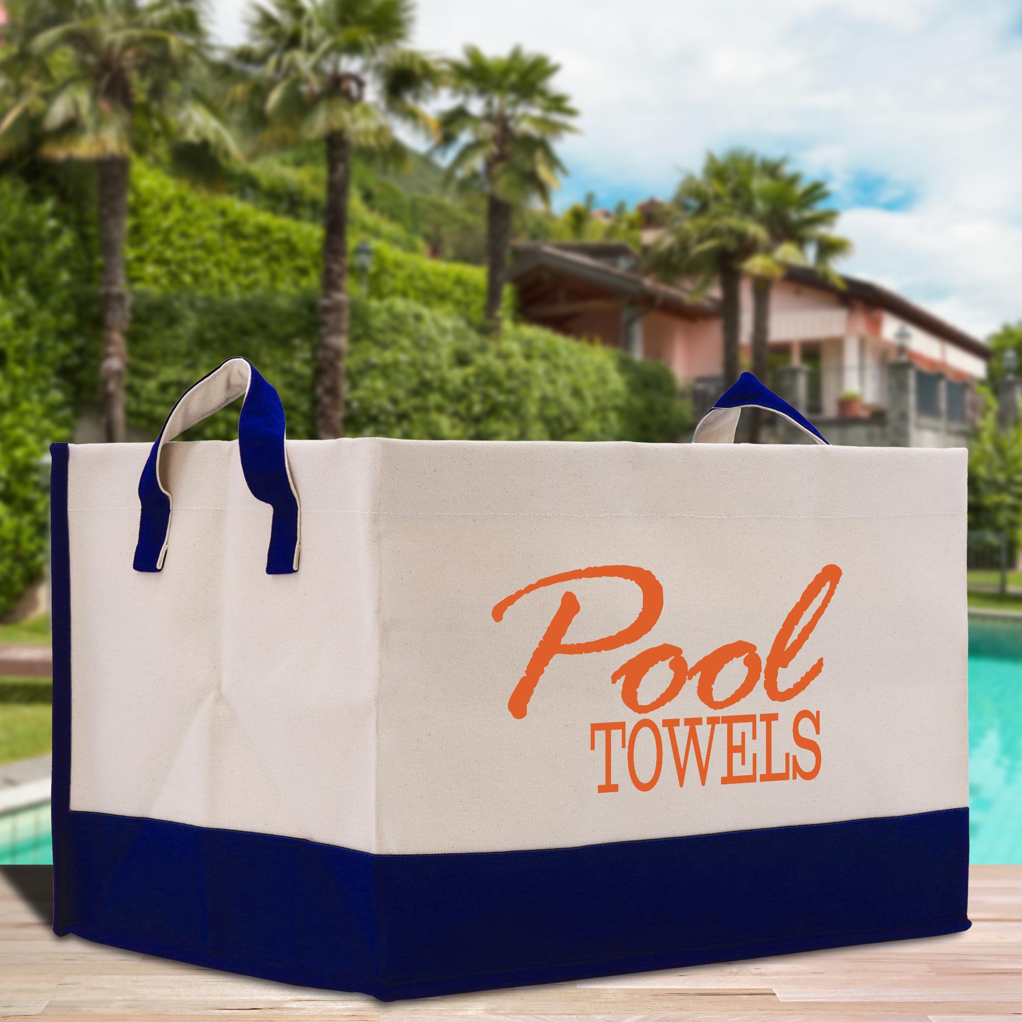 A large white and blue tote bag with the text &quot;Pool Towels&quot; printed on it, placed on a wooden surface near a pool with palm trees in the background.