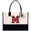 A beige tote bag with a black handle and a red embroidered letter "M" on the front.