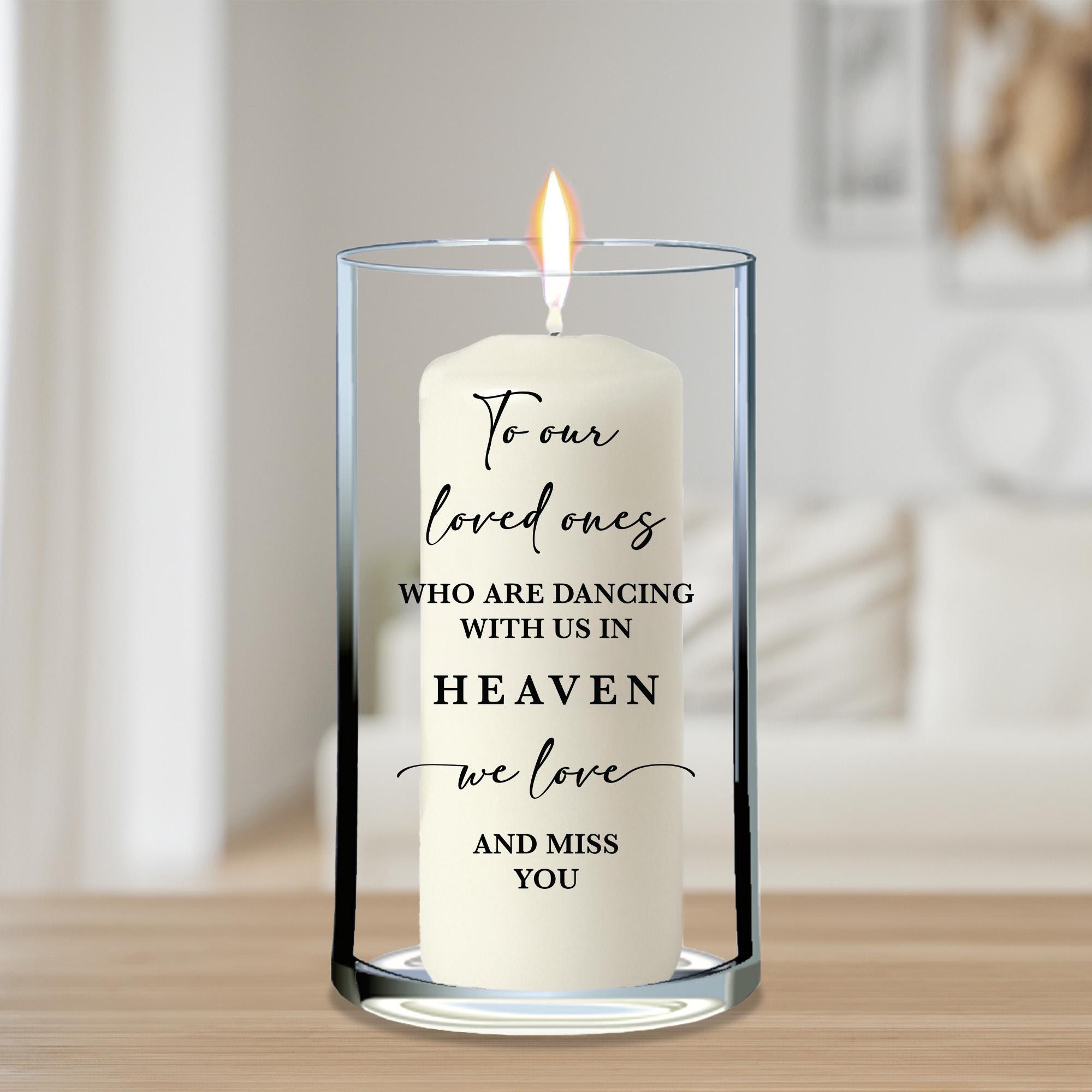 A white candle with a flame inside a glass vase, displaying a message about loved ones dancing in the sky.