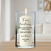 A white candle with a flame inside a glass vase, displaying a message about loved ones dancing in the sky.