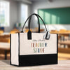 A white tote bag with black handles, featuring a colorful design and text that says "Mrs. Parker's Teacher Stuff".