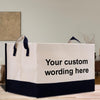 A white and black tote bag with the text "Your custom wording here" printed on it, placed on a wooden surface.