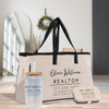 a beige tote bag with a black handle, a glass jar with a straw, and a small metal container on a wooden surface.