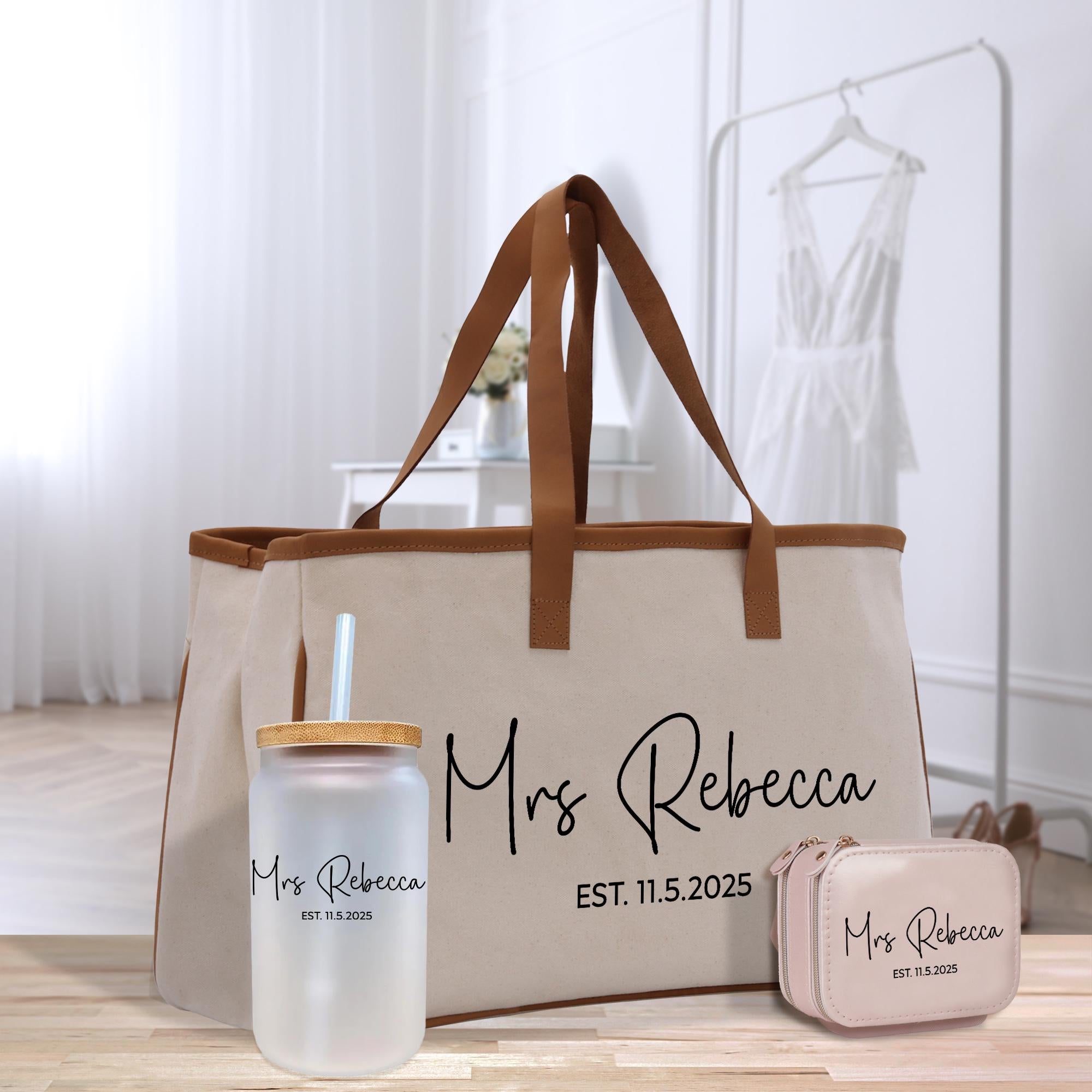 A beige tote bag with the name &quot;Mrs Rebecca&quot; printed on it, along with a straw cup and a small purse, all placed on a wooden surface.