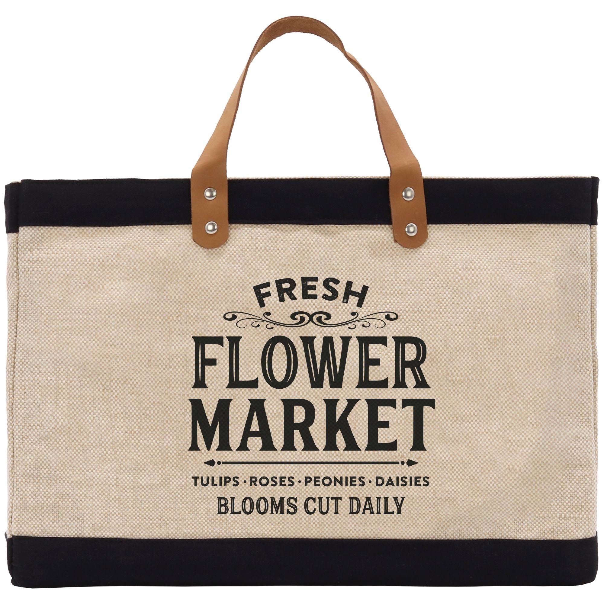 A beige tote bag with a black handle and strap, featuring a printed design that says &quot;FRESH FLOWER MARKET&quot; and lists various types of flowers such as tulips, roses, peonies, and daisies.