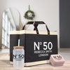 a black tote bag with the text "N°50 Rebecca Smith London" printed on it, along with a matching black and white glass jar with a straw and a pink box with the same text "N°50 Rebecca Smith London" printed on it.