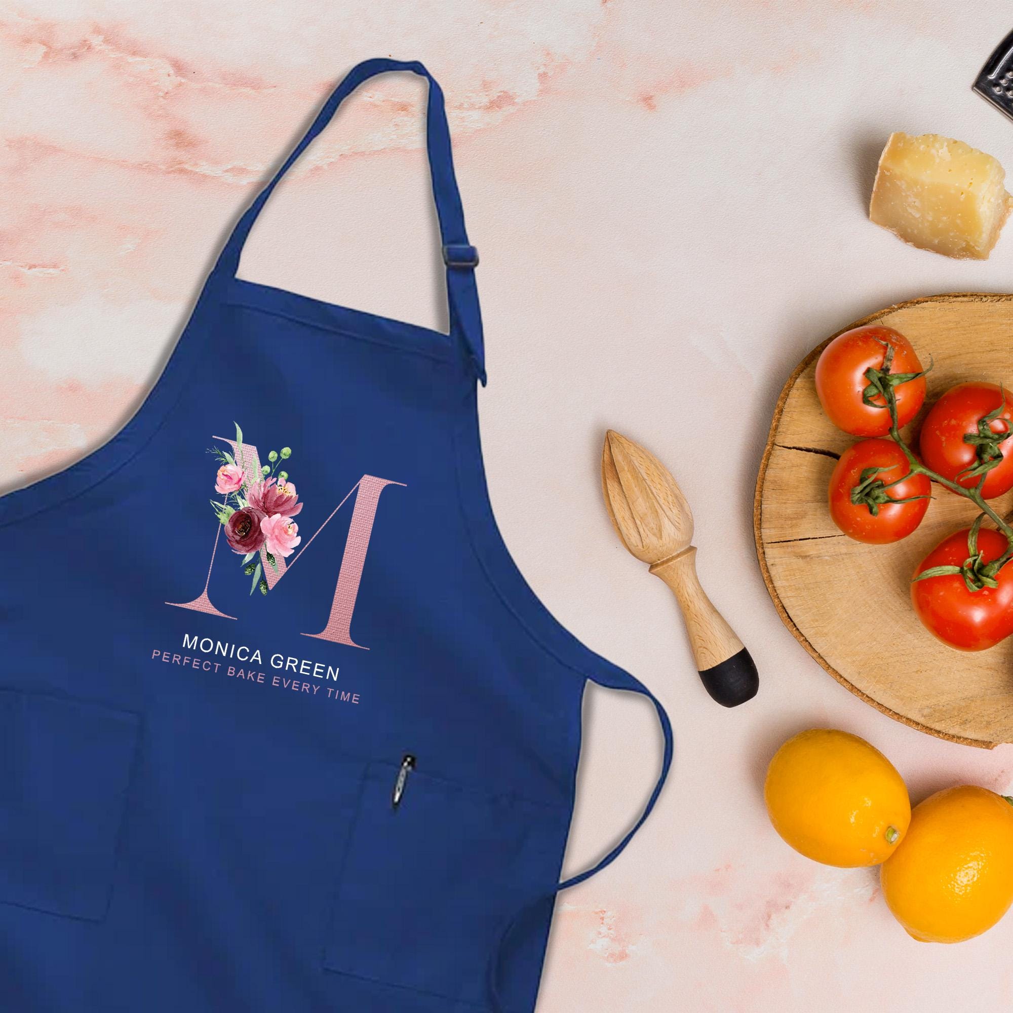 a blue apron with a floral design, a wooden juicer, a plate of tomatoes, and some oranges on a table.