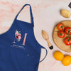 a blue apron with a floral design, a wooden juicer, a plate of tomatoes, and some oranges on a table.