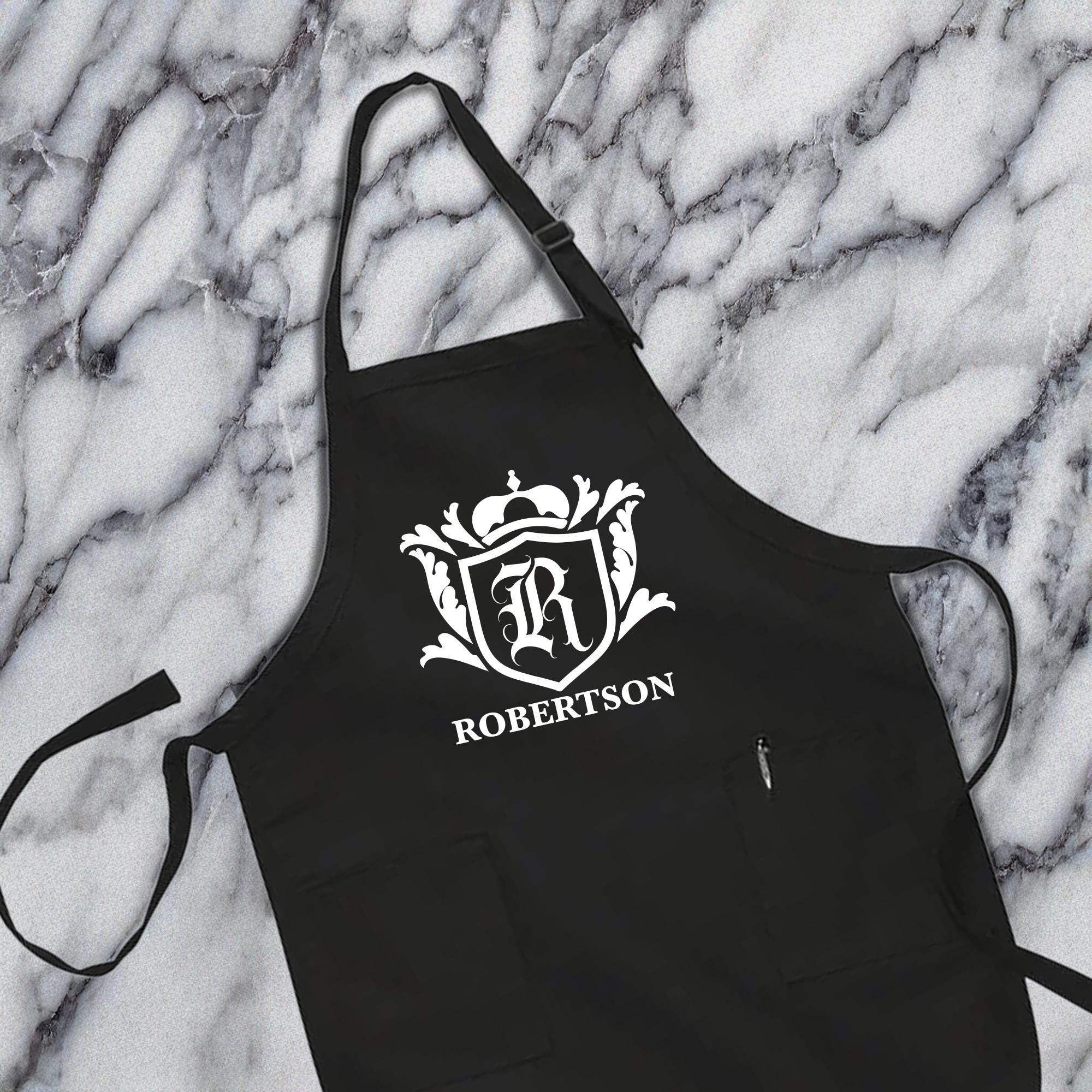 A black apron with a white crest and text on it, placed on a marble surface.