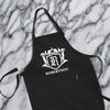 A black apron with a white crest and text on it, placed on a marble surface.