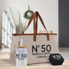 A beige tote bag with the text "N°50 Rebecca Smith London" printed on it, along with a straw cup and a small black box with the same text.