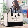 A large tote bag with a black and white design, featuring the text "Granny's Crochet & Crafts" printed on it. The bag is placed on a wooden surface, and there is a blurred figure of a woman in the background.