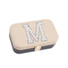 A beige jewelry box with a black lid, decorated with a large letter "M" made of pearls and rhinestones.