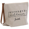 The image is a beige canvas tote bag with a zipper closure and a leather strap. It has a printed message on it that says "strengths and honor are her clothing" and the name "Judith" below it.