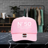A pink baseball cap with the text "N° 50 EMILY JOHNSON AUSTIN, TEXAS" printed on it, placed on a marble countertop.
