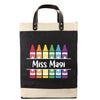 A black tote bag with a printed design of colorful crayons and the text 
