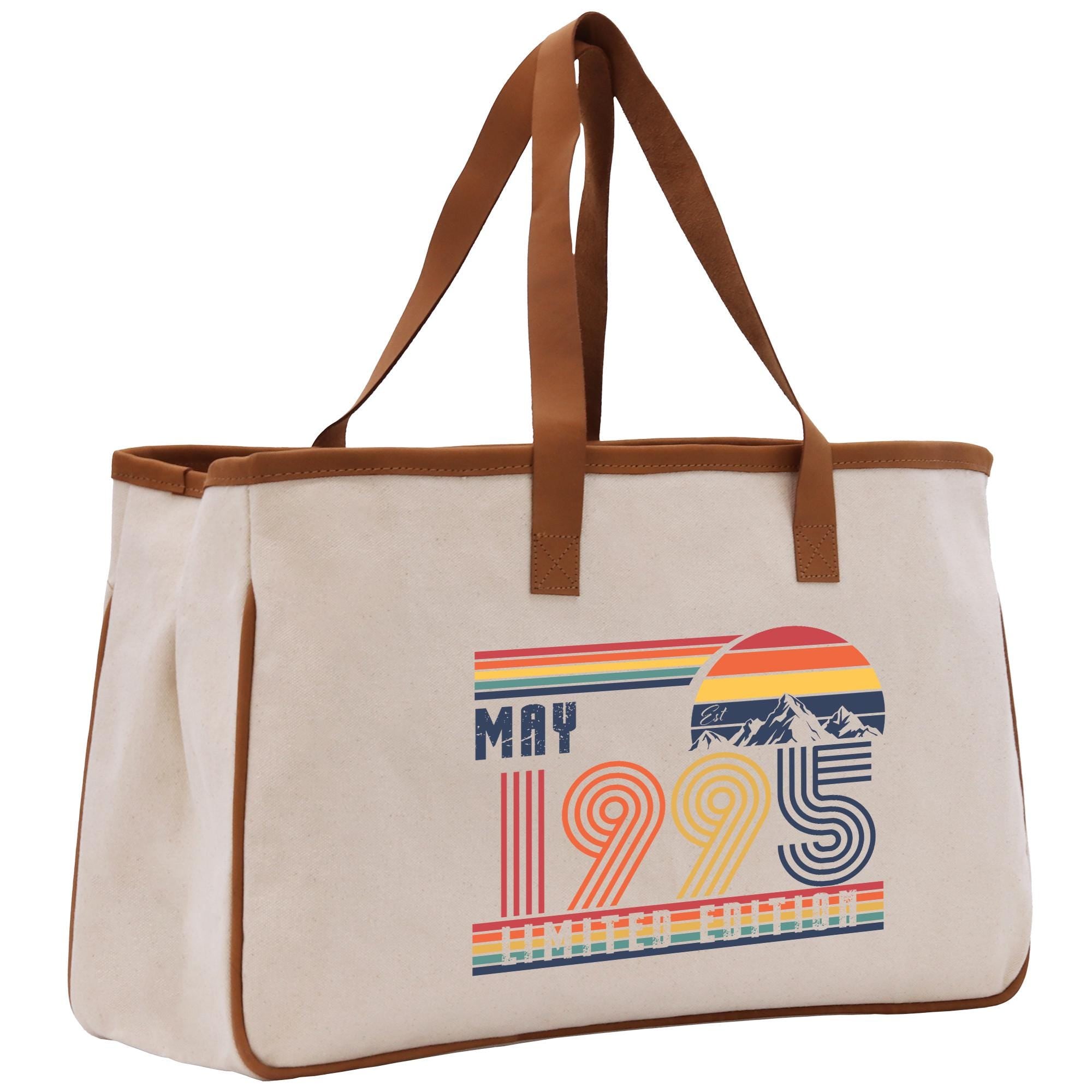 A beige canvas tote bag with a graphic design featuring the text "MAY 1995" and a mountain range.