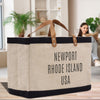 A beige tote bag with black trim and brown straps, featuring the text "NEWPORT RHODE ISLAND USA" printed on it.