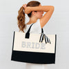 A woman with her hair in a ponytail is holding a large tote bag with the word "BRIDE" printed on it.