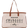 A beige canvas tote bag with a brown leather strap and the text "GOD SAYS YOU ARE" printed on it. Below the text, there are illustrations of flowers with descriptions of the corresponding Bible verse titles.