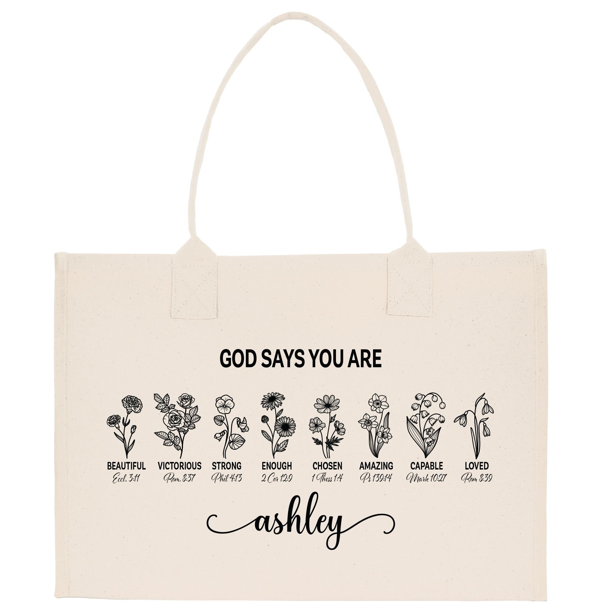A beige canvas tote bag with a printed design featuring various flower illustrations and the text &quot;God says you are Ashley&quot; printed on it.