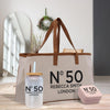 A beige tote bag with the text "N°50 Rebecca Smith London" printed on it, along with a straw cup and a small pink box.
