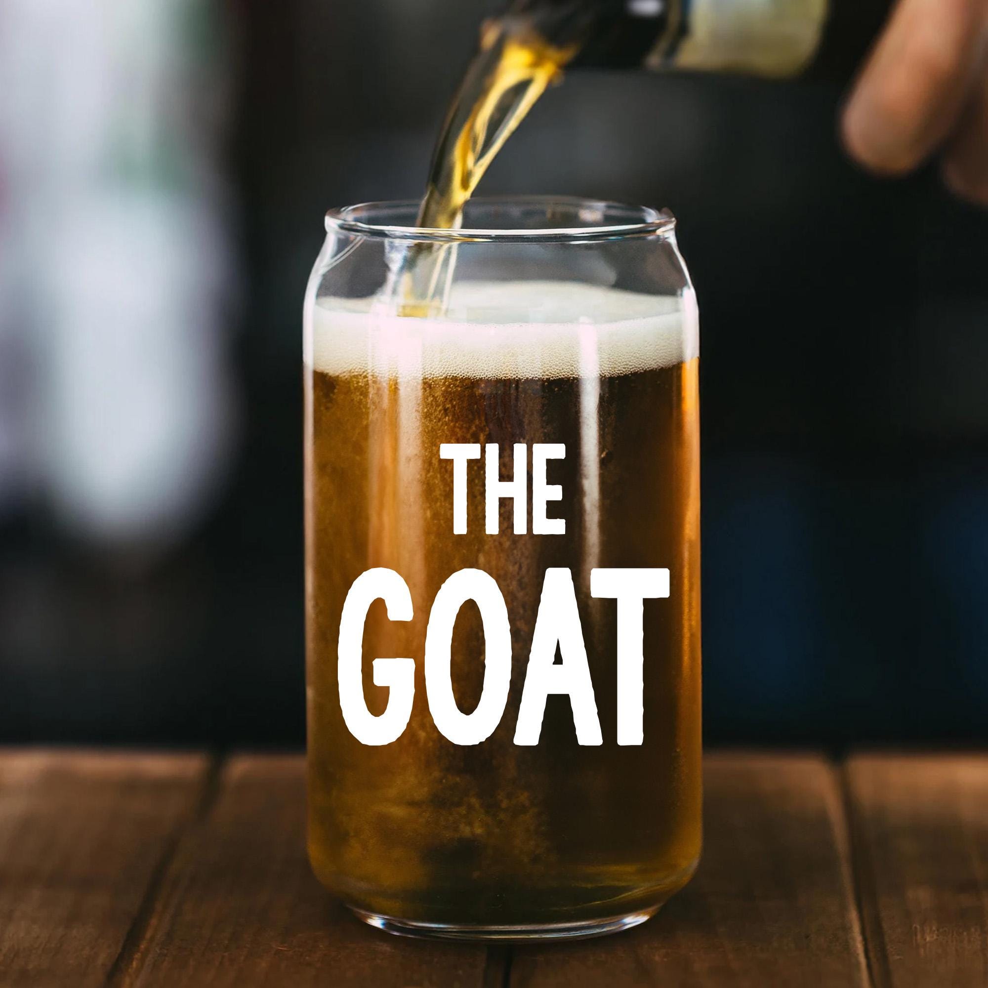 A glass of beer with a hand pouring liquid into it, with the text &quot;THE GOAT&quot; printed on the glass.