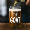 A glass of beer with a hand pouring liquid into it, with the text "THE GOAT" printed on the glass.