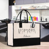 A large tote bag with a black and white design featuring various hair styling tools, such as scissors, combs, and hair dryers, printed on it. The bag has a black handle and a white trim.