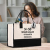A large tote bag with a black and white design, featuring text and a tag, placed on a wooden surface.