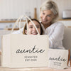 A smiling woman and a young girl are sitting together in a kitchen, with a large tote bag in the foreground that says "auntie" and "JENNY EST 2025".