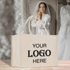 A beige tote bag with the text "YOUR LOGO HERE" printed on it, placed on a wooden surface. In the background, there is a blurred image of a woman wearing a white wedding dress.