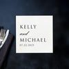 A white square card with black text is placed on a dark surface next to a fork and knife.