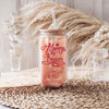 A glass jar with a straw, featuring a red and white design, sits on a woven mat.