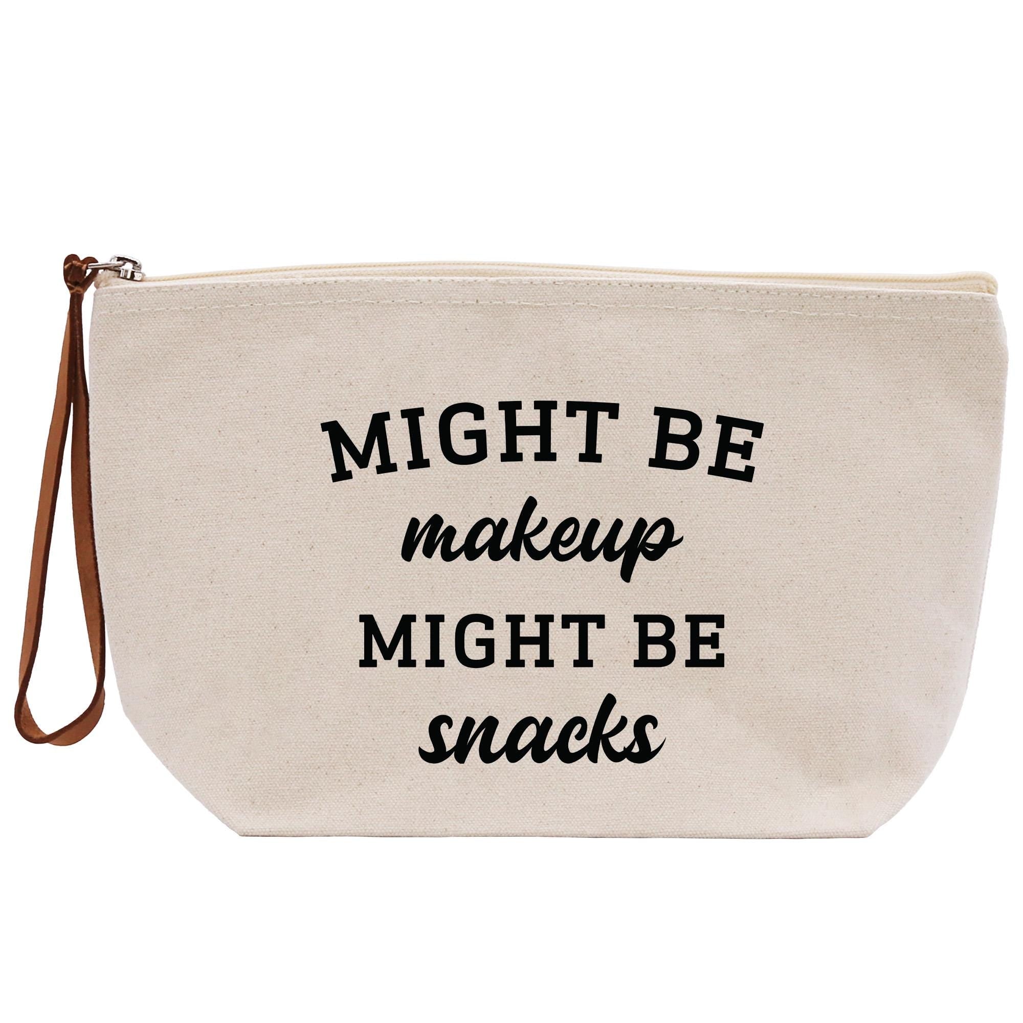 A beige canvas makeup bag with the text &quot;MIGHT BE makeup MIGHT BE snacks&quot; printed on it.