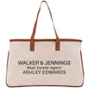 A beige canvas tote bag with brown straps and text printed on it.