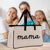 A large canvas tote bag with the word "mama" printed on it, placed in front of two smiling women.