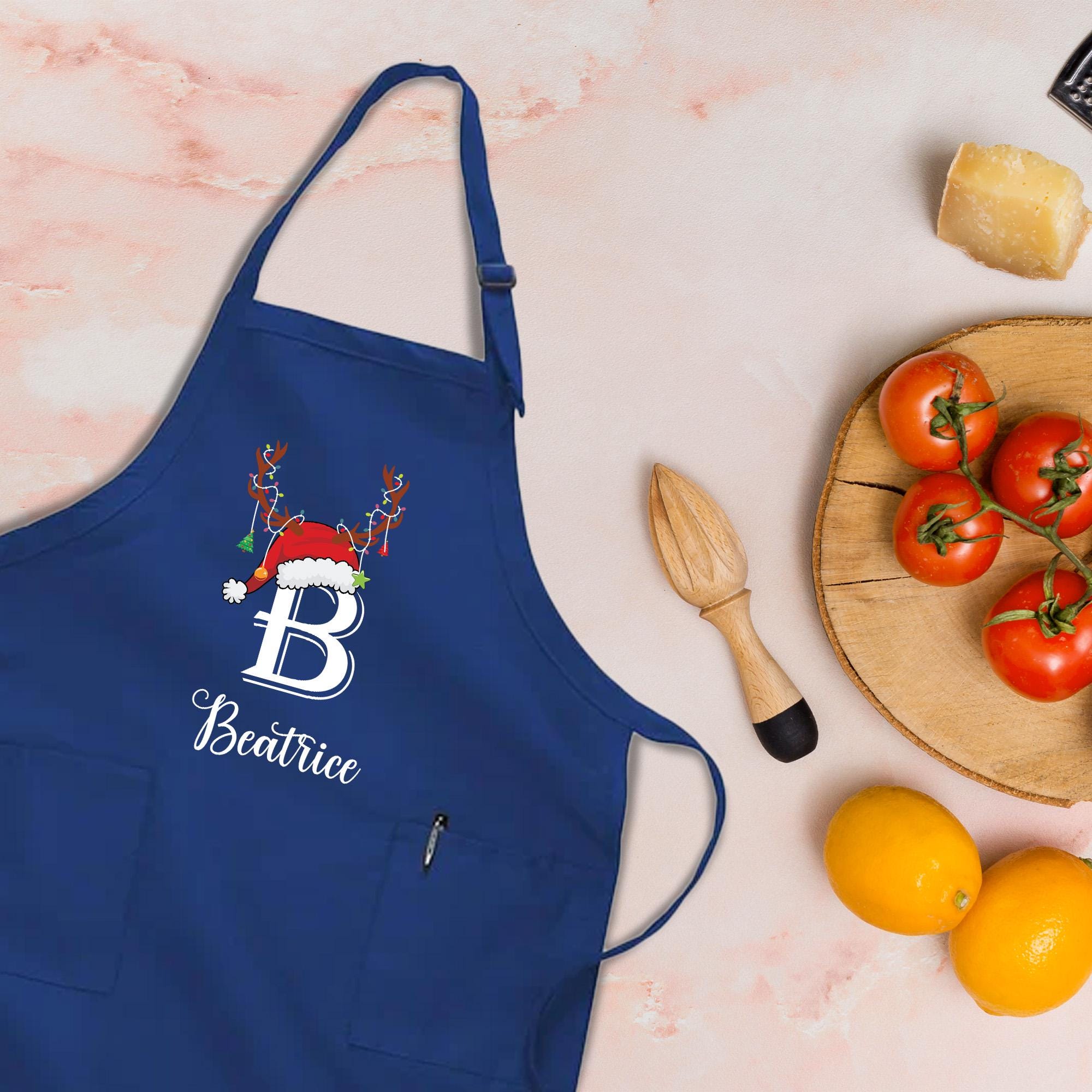 A blue apricot with a white letter &quot;B&quot; and the name &quot;Beattrice&quot; printed on it, along with a wooden juicer and a plate of tomatoes and oranges.