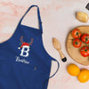 A blue apricot with a white letter "B" and the name "Beattrice" printed on it, along with a wooden juicer and a plate of tomatoes and oranges.